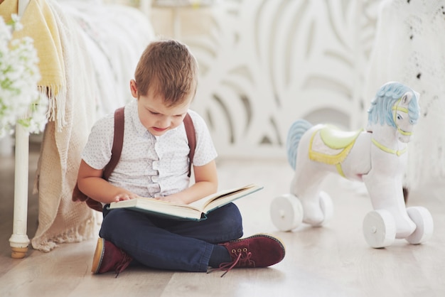 Il ragazzino carino sta andando a scuola per la prima volta. Bambino con zaino e libro. Il bambino fa una valigetta, stanza dei bambini