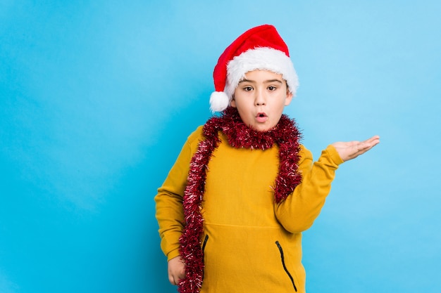 Il ragazzino che celebra il giorno di Natale che porta un cappello di Santa ha isolato lo spazio impressionato della copia della tenuta sulla palma.