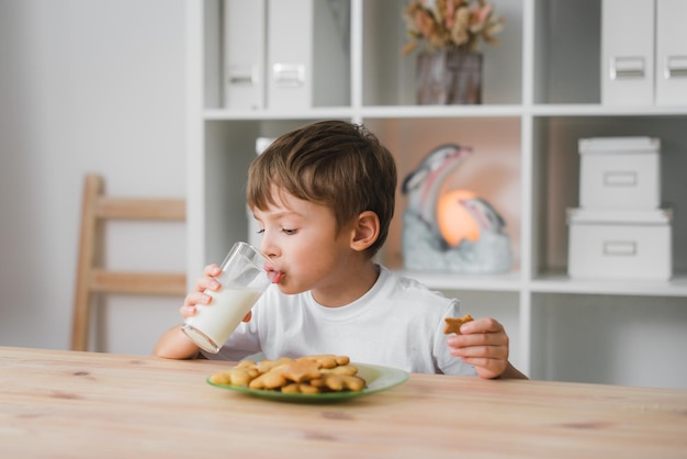 Il ragazzino che cucina in casa sta mangiando al tavolo della cucina e mangiando biscotti freschi fatti in casa con gusto