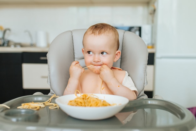 Il ragazzino che mangia gli spaghetti sembra affamato e il sugo per la pasta gli scompiglia tutto il viso mentre fa il...