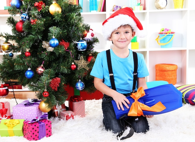 Il ragazzino con il cappello di Babbo Natale si siede vicino all'albero di Natale con le pinne