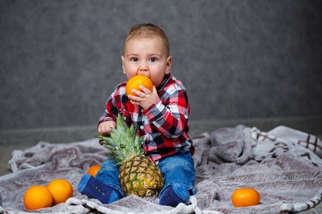 Il ragazzino con la maglietta si siede sul plaid e tiene la frutta