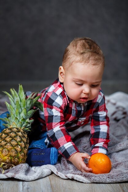 Il ragazzino con la maglietta si siede sul plaid e tiene la frutta