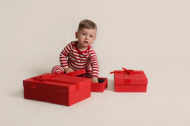 il ragazzino con una giacca a righe e pantaloni rossi siede su uno sfondo bianco con coriandoli e scatola regalo