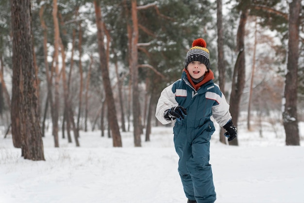 Il ragazzino corre allegramente attraverso la neve. Il bambino gioca nella foresta invernale su sfondo di grandi abeti.