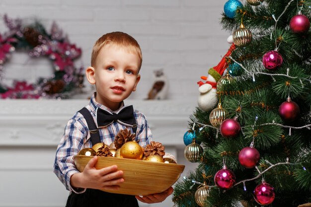 Il ragazzino decora un albero di Natale all'interno con decorazioni natalizie