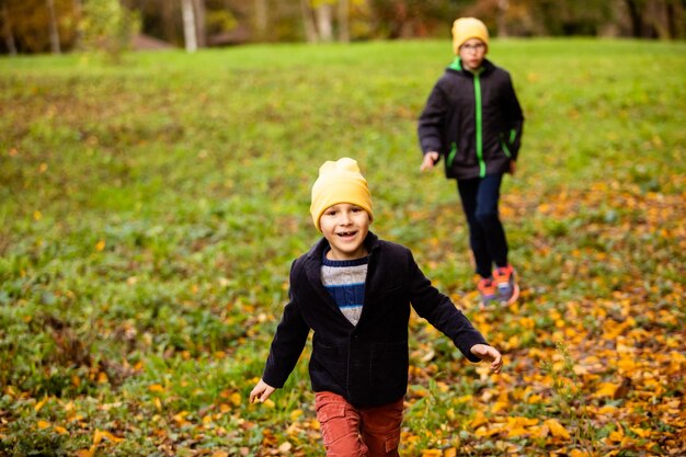 Il ragazzino divertente e sorridente cammina con un amico nel parco autunnale I ragazzi sono vestiti con giacche leggere e cappelli