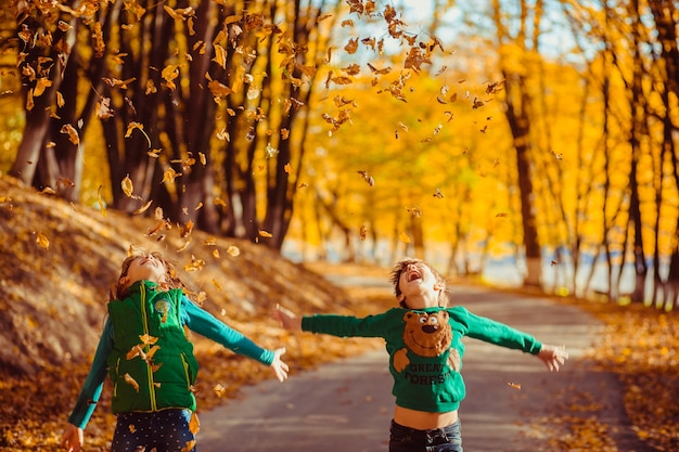 Il ragazzino e la ragazza felici si divertono con le foglie cadute nel parco di autunno