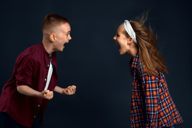 Il ragazzino e la ragazza stanno gridando a vicenda, sviluppando l'effetto dei capelli. Bambini e vento, bambini isolati su sfondo scuro, emozione del bambino