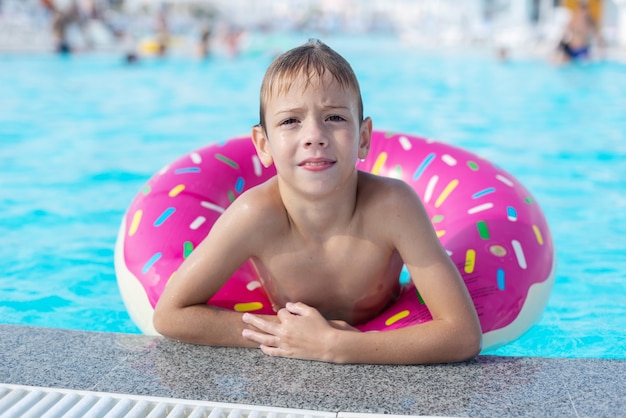 Il ragazzino felice con l'anello di vita variegato sotto forma di ciambella si diverte in piscina