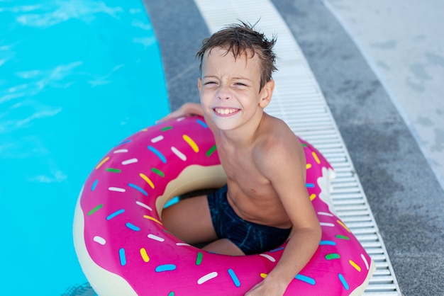 Il ragazzino felice con l'anello di vita variegato sotto forma di ciambella si diverte in piscina
