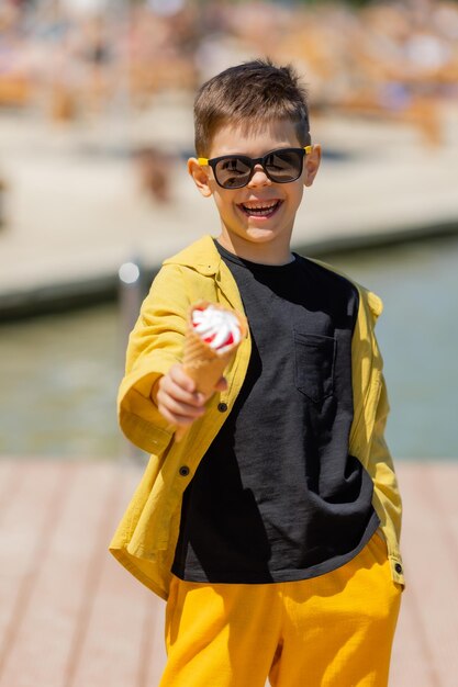 Il ragazzino felice mangia il gelato in un cono di cialda in estate durante una passeggiata