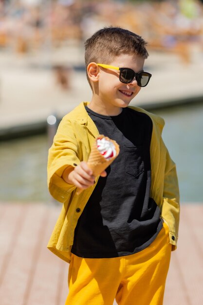 Il ragazzino felice mangia il gelato in un cono di cialda in estate durante una passeggiata