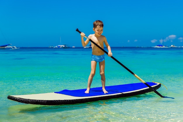 Il ragazzino felice si diverte su un paddleboard nel mare tropicale