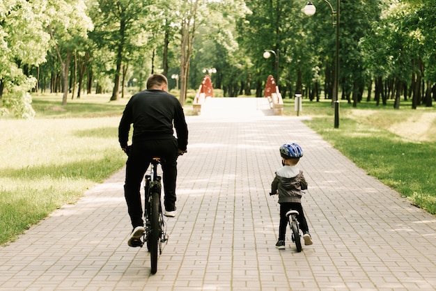 Il ragazzino felice va in bicicletta con un giovane papà nel parco