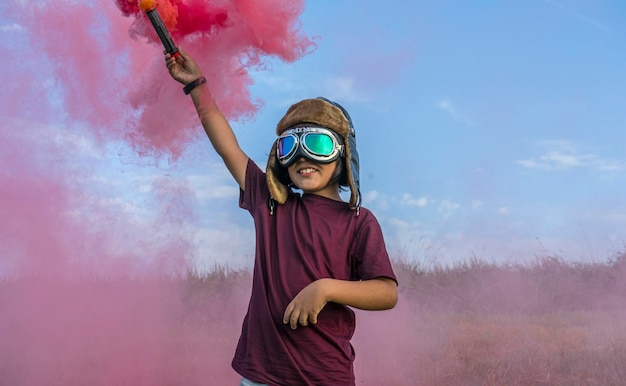 Il ragazzino gioca con il fumo colorato, indossando un cappello da aviatore degli anni '20 e occhiali da pilota di aeroplano