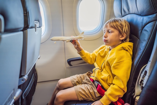 Il ragazzino gioca con l'aereo giocattolo nell'aereo a reazione commerciale che vola in vacanza