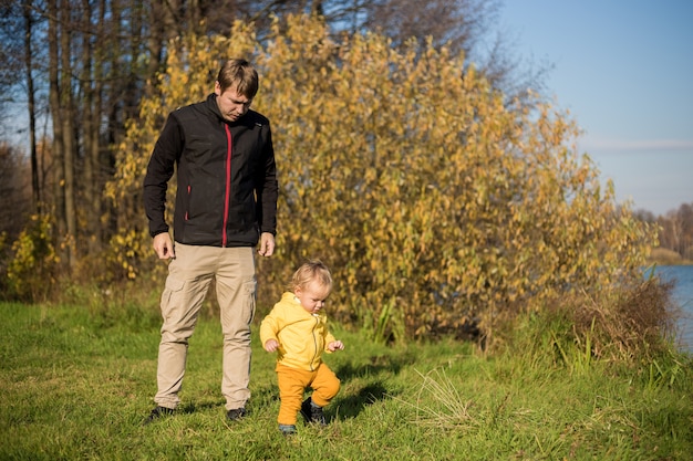 Il ragazzino impara a camminare, papà si prende cura di lui sullo sfondo della foresta autunnale e del lago