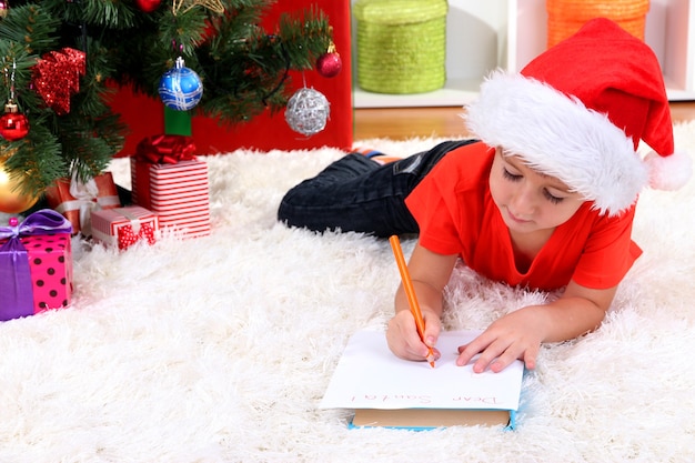 Il ragazzino in cappello della Santa scrive la lettera a Babbo Natale