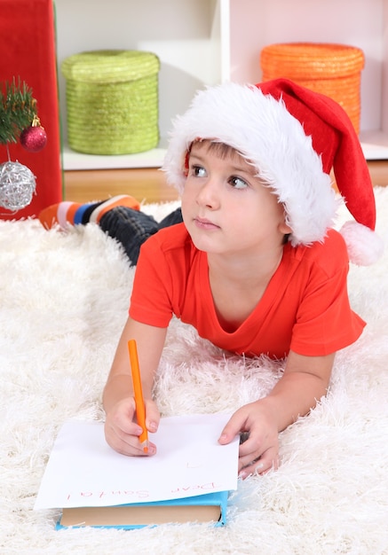 Il ragazzino in cappello della Santa scrive la lettera a Babbo Natale