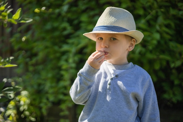 Il ragazzino in cappello di paglia alla moda raccoglie la bacca del caprifoglio