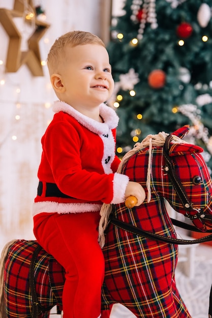 Il ragazzino in costume della santa guarda in alto e sorride. baby sitter su cavallo a dondolo.