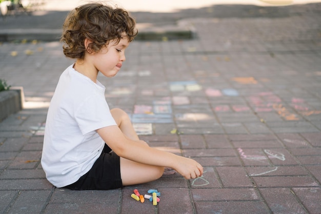Il ragazzino in età prescolare disegna con gessetti colorati per terra