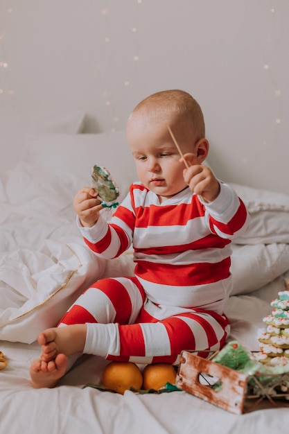 Il ragazzino in pigiama rosso e bianco mangia un bel biscotto di Natale fatto in casa seduto a letto con un cane. bambino e animale domestico. stile di vita. Foto di alta qualità