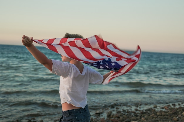 Il ragazzino lascia sventolare la bandiera americana nelle sue mani sul vento al mare