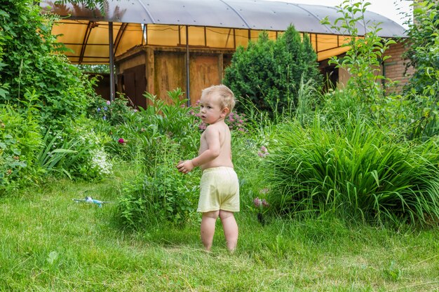 Il ragazzino si trova su un prato verde nel giardino di una casa di campagna.