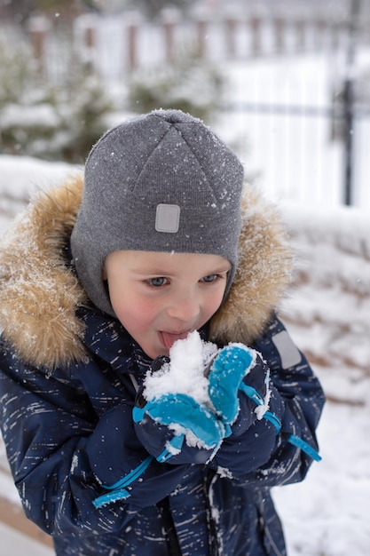 Il ragazzino sveglio cerca di mangiare la neve con la lingua in inverno per strada