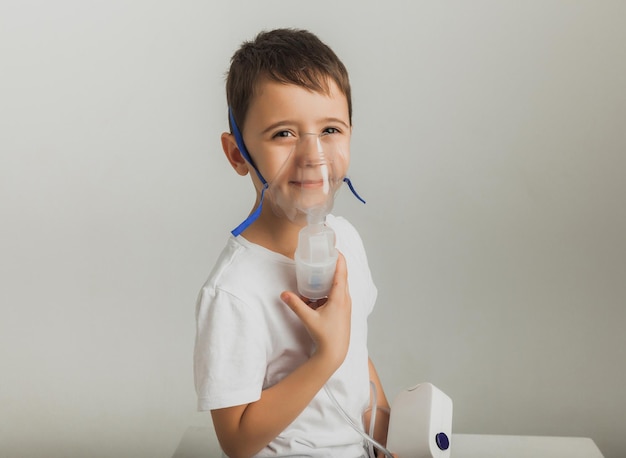 Il ragazzino sveglio fa l'inalazione. Il bambino tiene in mano un inalatore e viene curato per la tosse. foto in studio di alta qualità.