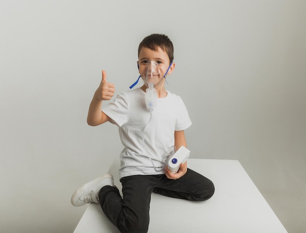 Il ragazzino sveglio fa l'inalazione. Il bambino tiene in mano un inalatore e viene curato per la tosse. foto in studio di alta qualità.