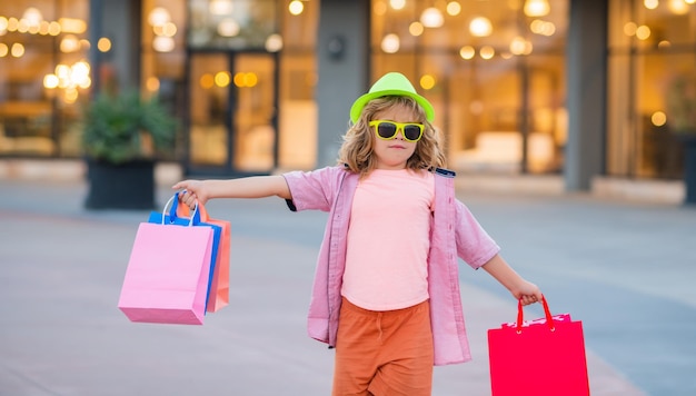Il ragazzino sveglio in abiti di moda estivi va a fare shopping bambino felice con i pacchetti della spesa nelle mani