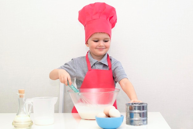 Il ragazzino sveglio in un cappello da chef rosso impasta l'impasto della pasticceria in una ciotola. Torte fatte in casa.