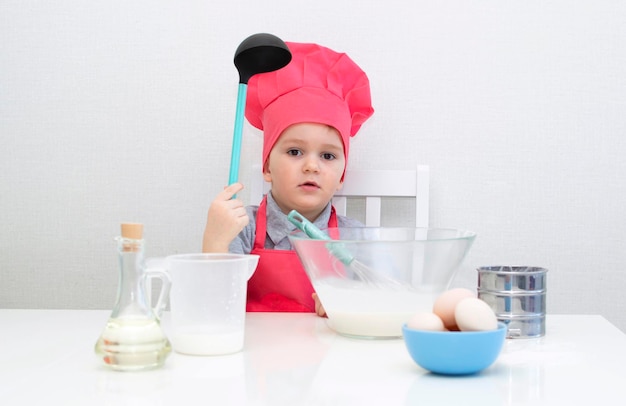 Il ragazzino sveglio in un cappello da chef rosso impasta l'impasto della pasticceria in una ciotola. Torte fatte in casa.