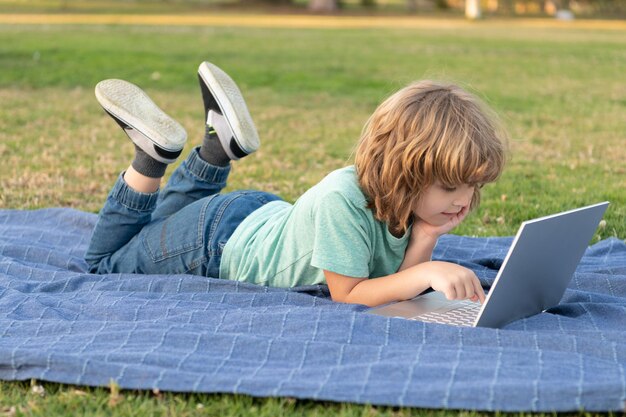 il ragazzino usa un moderno laptop wireless sull'erba del parco, studia online.