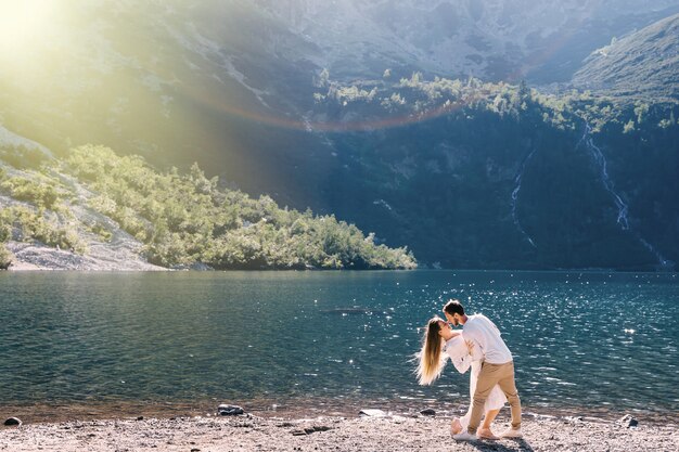 Il ragazzo abbraccia la ragazza e lei si piega all'indietro sulla riva del lago