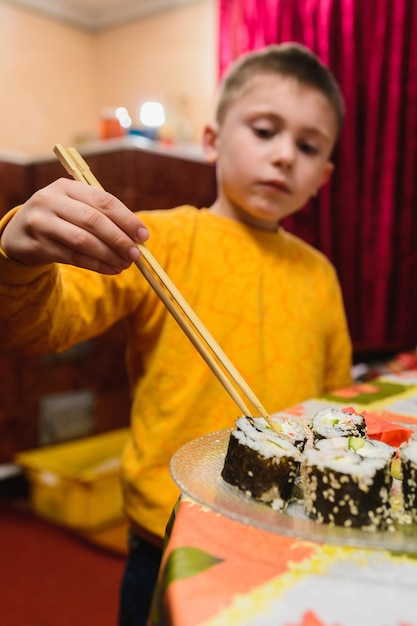 Il ragazzo adolescente prende il rotolo di sushi del piatto da mangiare