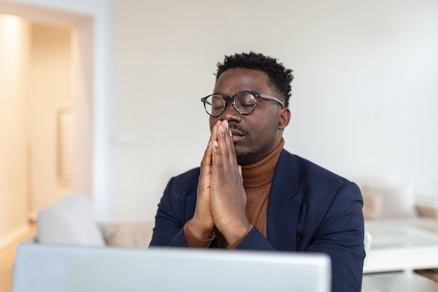 Il ragazzo africano si siede alla scrivania con i palmi chiusi e gli occhi chiusi pensando alla soluzione del problema di ricerca