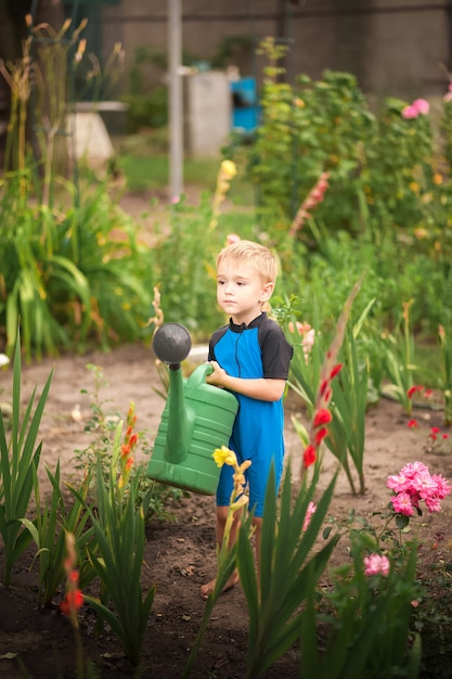 Il ragazzo aiuta con il giardino estivo. Giochi per bambini con acqua nel cortile.