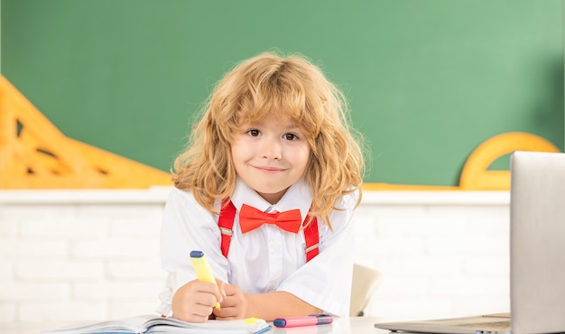 Il ragazzo allegro del bambino nello studio del farfallino nella classe scolastica alla lavagna, scuola.