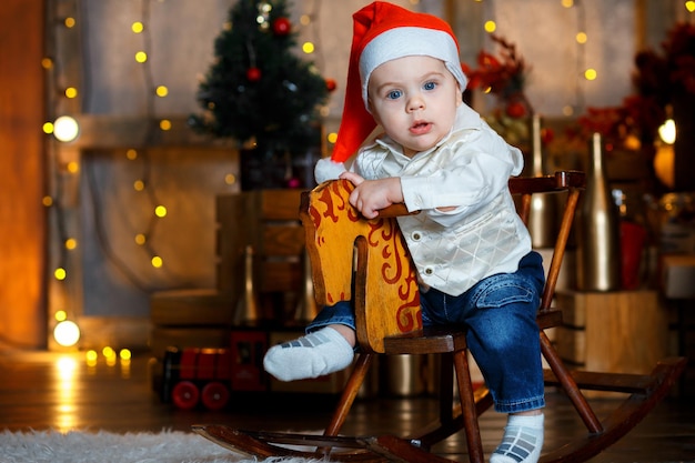 Il ragazzo allegro si siede su un cavallo giocattolo vicino a un albero di Natale in uno studio decorato a festa