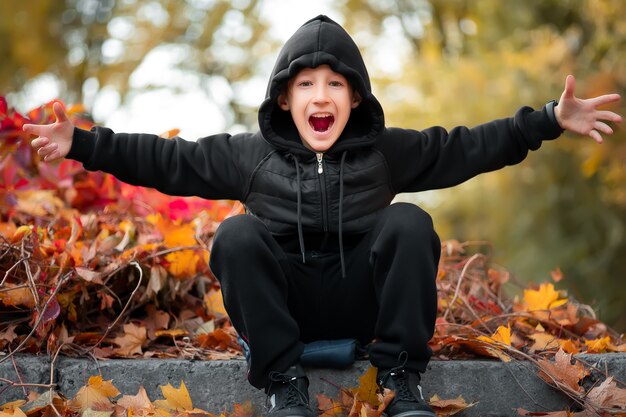 Il ragazzo allegro si siede sul confine nel bellissimo parco autunnale.