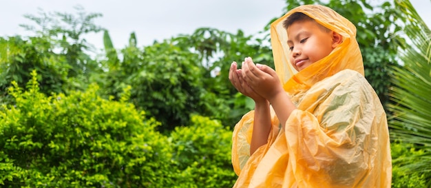 Il ragazzo asiatico che indossa l'impermeabile arancione è felice e si diverte sotto la pioggia in una giornata piovosa