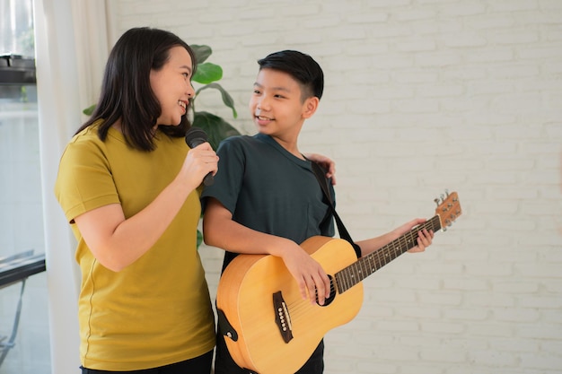 Il ragazzo asiatico che suona la chitarra e la madre cantano una canzone e si abbracciano si sentono apprezzati e incoraggiati