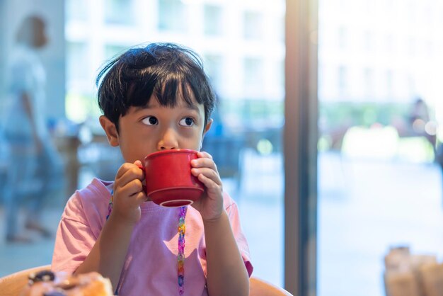 Il ragazzo asiatico dai capelli neri in una camicia rosa è felice di mangiare la colazione in vacanza al ristorante del resort