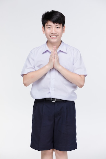 Il ragazzo asiatico del bambino in uniforme dello studente, comportandosi sawaddee significa ciao.