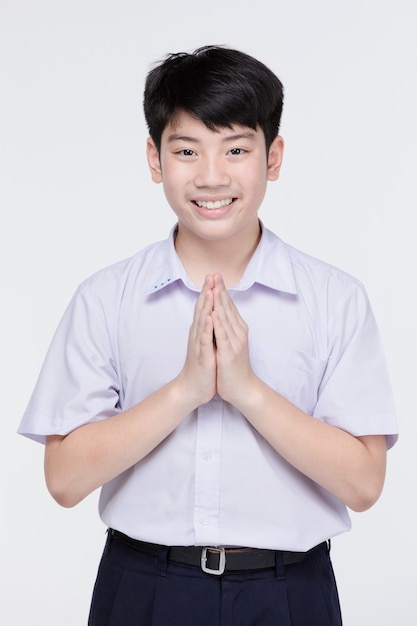 Il ragazzo asiatico del bambino in uniforme dello studente, comportandosi sawaddee significa ciao.