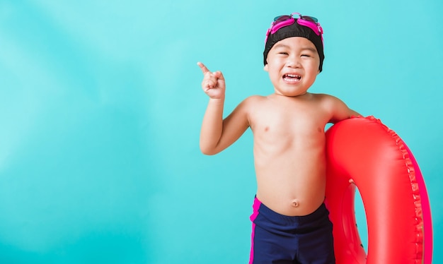 Il ragazzo asiatico felice del bambino piccolo indossa gli occhiali di protezione e il costume da bagno tiene l'anello gonfiabile dell'anguria